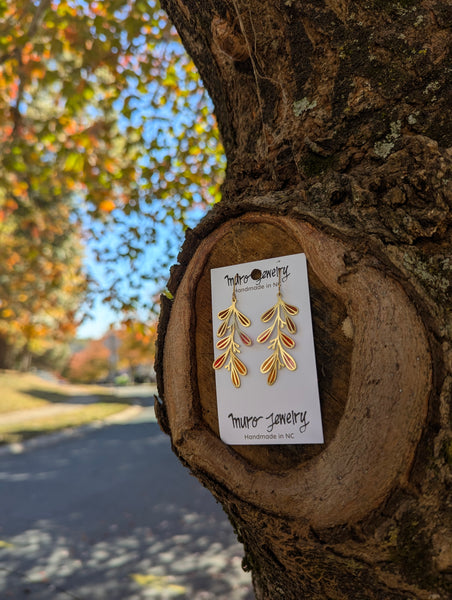Gold leaf earrings on a card with 'Murn Jewelry' branding, displayed against a tree background.