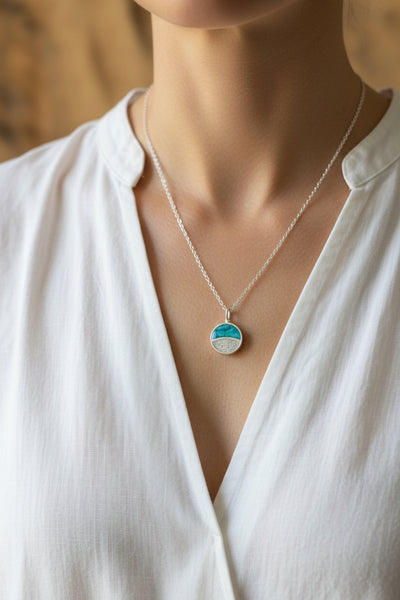 Silver necklace with a blue and white pendant on a white stand with wooden background