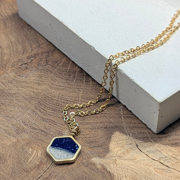 Gold necklace with a blue pendant on a wooden surface