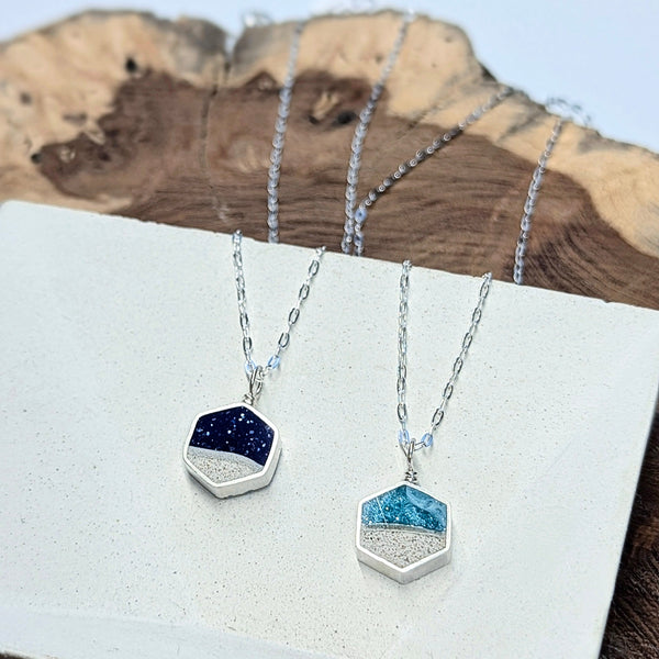 Two silver necklaces with blue hexagonal pendants on a wooden surface.