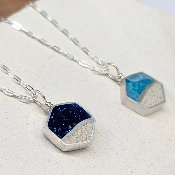 Two hexagonal pendant necklaces with blue and silver colors on a light surface.